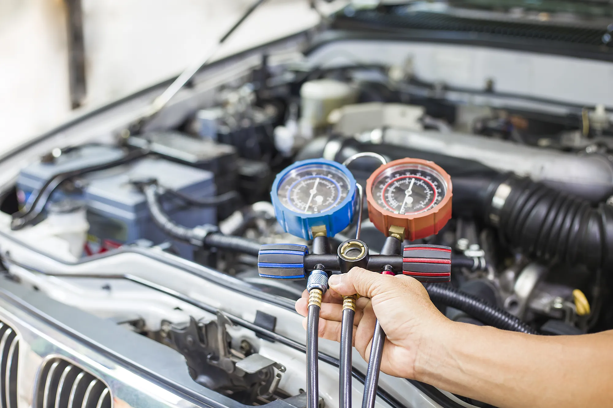 Technician checking car air conditioning pressures with gauges during a regas in Epping