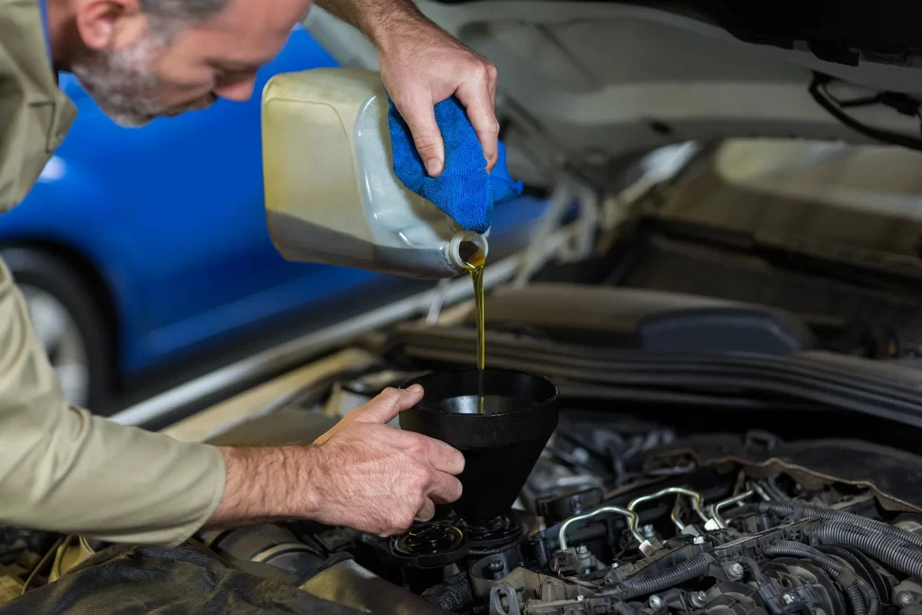 Technician pouring engine oil into a car engine during a service